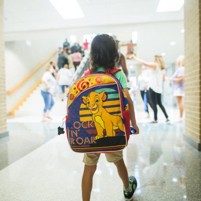 Unrecognizable child with backpack walking in crowded hall